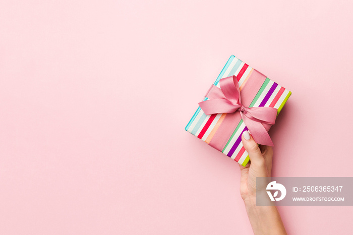 Females hands holding striped gift box with colored ribbon on living coral background. Christmas co