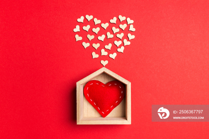 Top view of red textile heart in a wooden house decorated with small hearts on colorful background. 