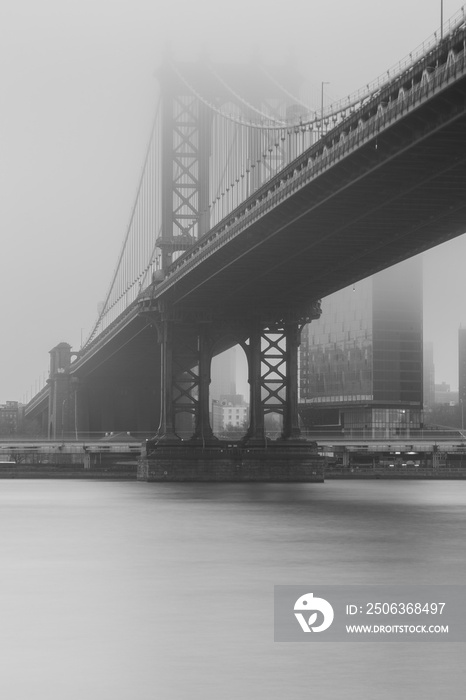 Black and white photo of Manhattan Bridge from east river on a foggy day with long exposure