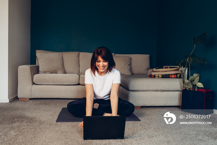 Woman is doing online yoga with laptop during self isolation at her living room, online education, d