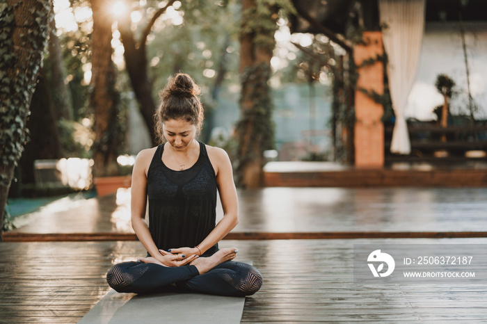 Concentrated girl sitting in lotus pose and meditating or praying. Young woman practicing yoga alone