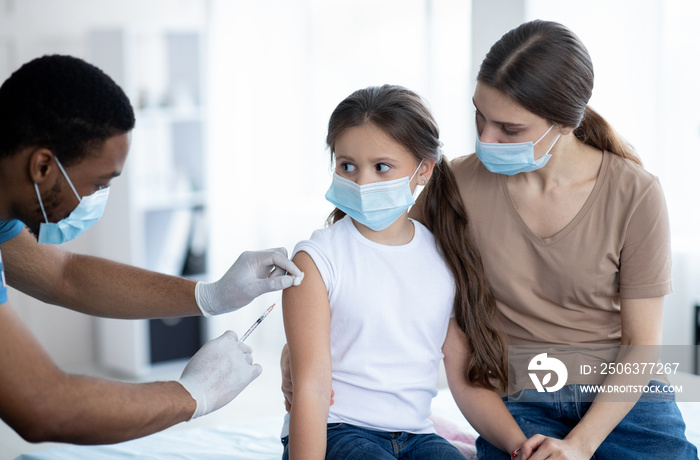 Mother and daughter in medical masks getting vaccinated against covid-19, doctor giving injection of