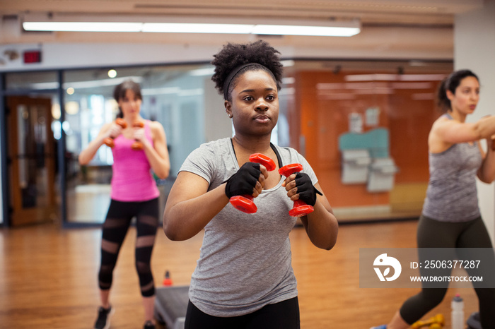 Confident female athletes exercising with dumbbells while standing in gym