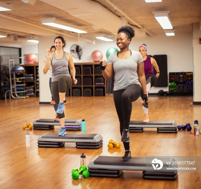 Smiling female athletes exercising on aerobic steps in gym