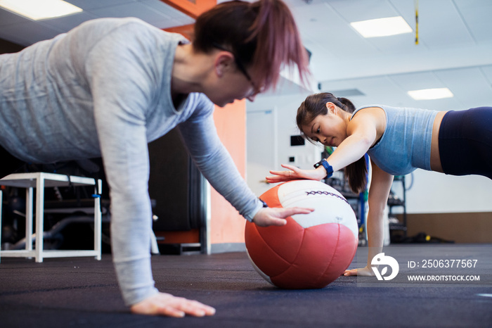 Side view of female athletes exercising with medicine ball on floor in gym