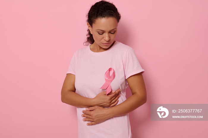 一位非裔美国女性将双手放在粉色T恤上的粉色缎带下，参加乳腺癌症运动，