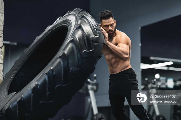 Shirtless muscular guy flipping huge tire at gym