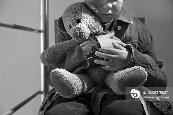 Homeless little boy with teddy bear sitting indoors