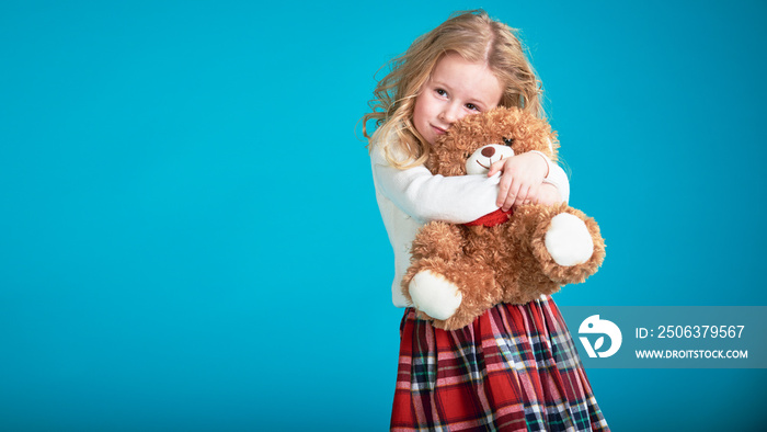 可爱的小女孩拥抱着棕色泰迪熊。