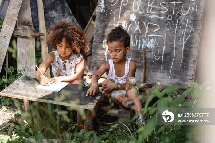 selective focus of african american kid writing near brother sitting with dirty teddy bear