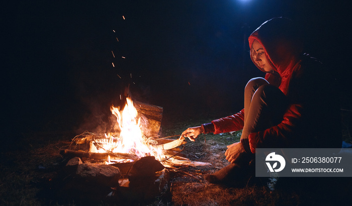 Young woman in sitting near the campfire at cold night