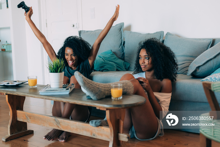快乐的年轻两个黑人女人坐在沙发上玩电子游戏。