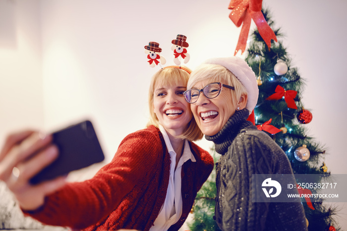 Cute caucasian woman and her mother taking selfie in front of decorated christmas tree. Christmas ti