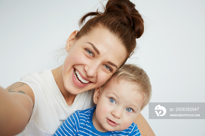 Young mother with her one years old little son dressed in pajamas are posing. Mom with son taking se