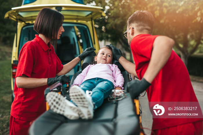 Doctors with injured little girl in front of ambulance car.