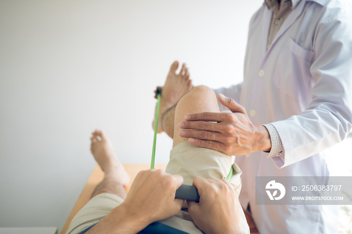 Confident physical therapist helps patient use resistance band stretching out his leg in clinic room