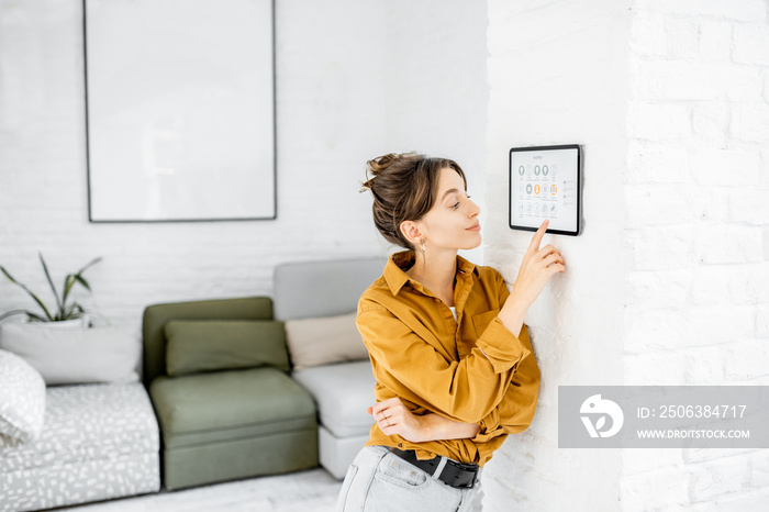 Woman controlling home with a digital touch screen panel installed on the wall in the living room