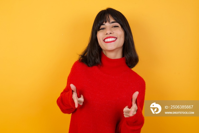 Joyful and charismatic Caucasian brunette woman wearing red casual sweater isolated over yellow back