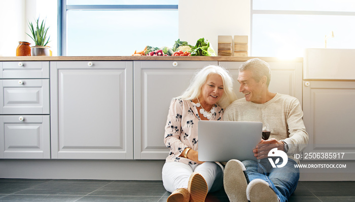 Senior people using laptop in kitchen.