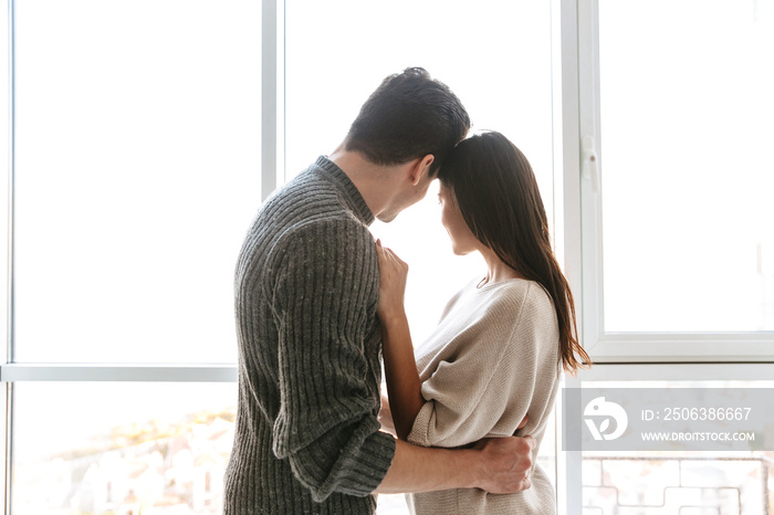 Happy young couple hugging while standing at the window