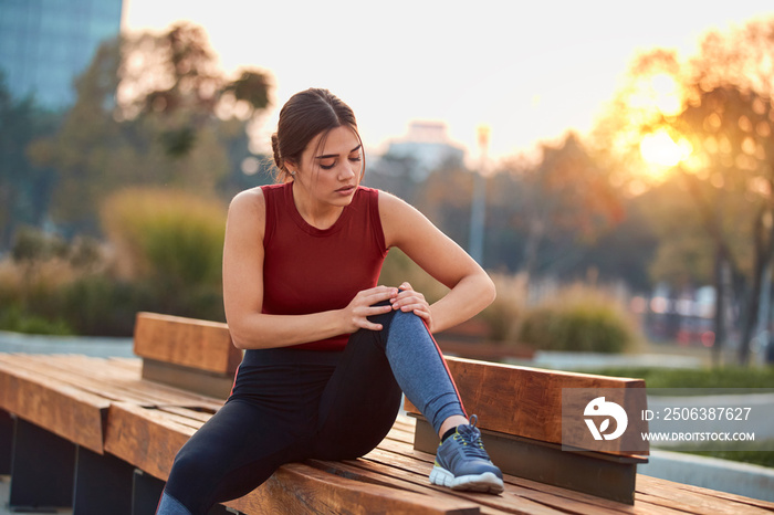 Young sportswoman having pain / injury during exercise and jogging in the park.