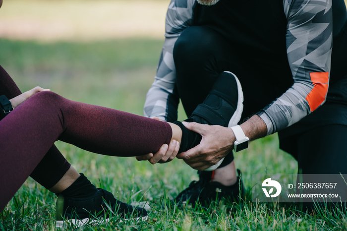 cropped view of sportsman touching injured leg of sportswoman sitting on lawn