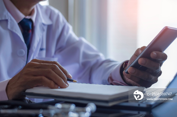 Male doctor hand holding and using mobile smart phone ,work on laptop computer with cup of coffee on