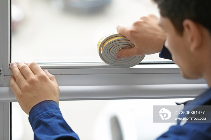 Young worker applying rubber strip onto window in office