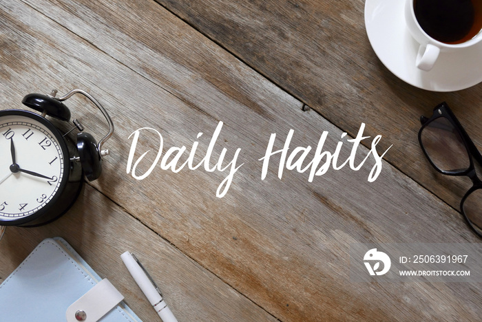 Top view of clock,notebook,pen,glasses and coffee on wooden background written with Daily Habits.