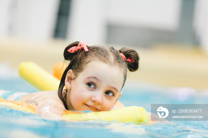 小女孩在游泳池里拿着黄色的面条游泳。