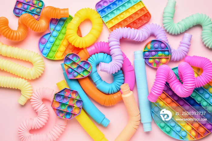 粉色背景下的彩色Pop Tubes和Pop-it坐立不安的玩具