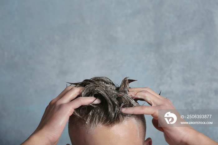 Young handsome man washing hair on gray background