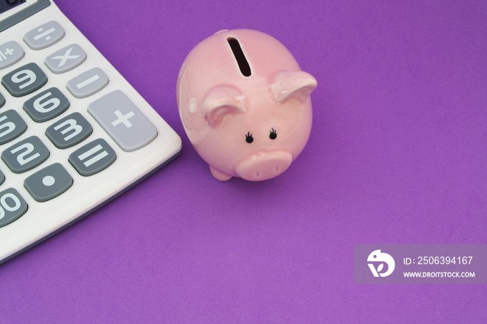 Piggy bank and calculator on purple background, save money concept