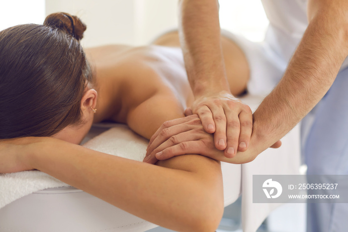 Relaxed woman getting medical body massage done by professional physiotherapist in modern clinic