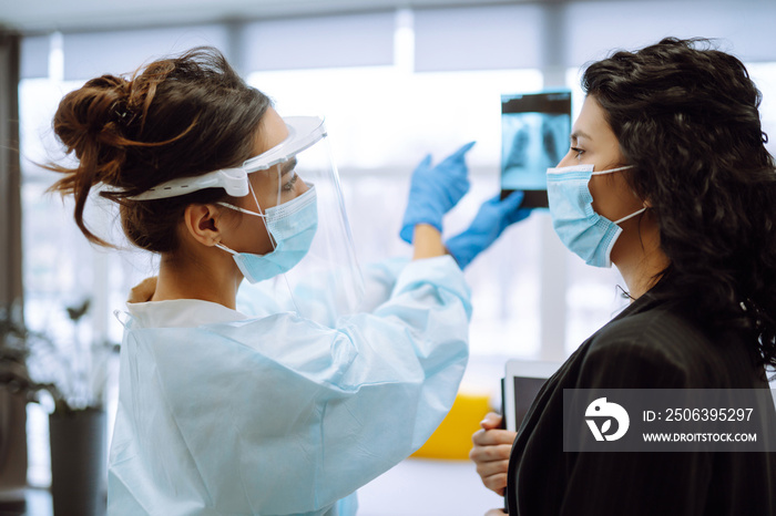 A female doctor in visor and protective gloves  discussing an x-ray. Doctor  examines an X-ray of a 