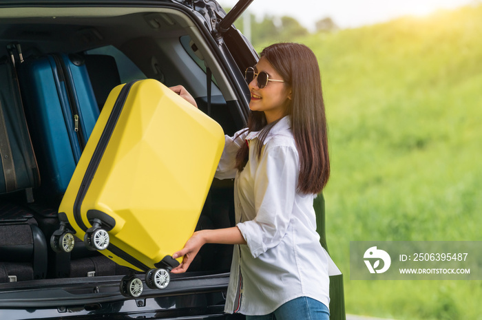 亚洲女子在长周末旅行中将黄色行李箱抬进SUV车。人们的生活方式