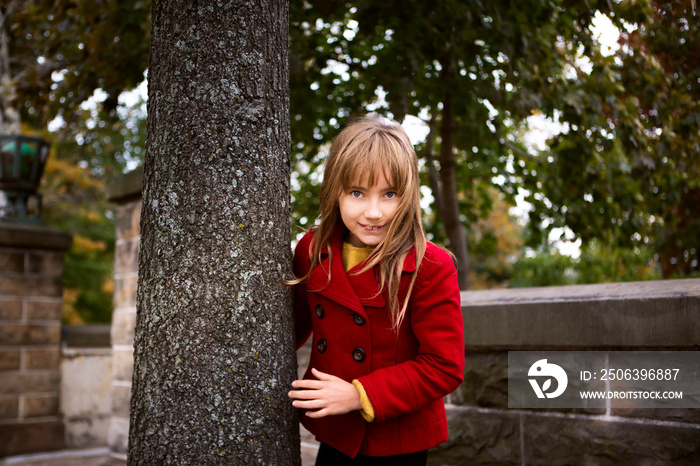 Portrait of happy girl standing by tree trunk in park