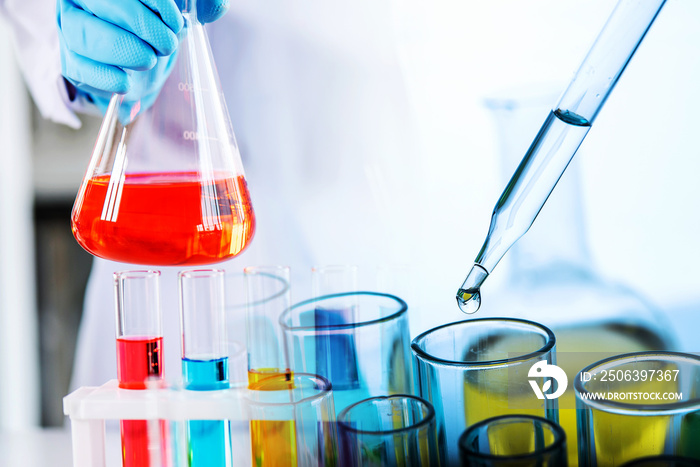 hand of scientist holding flask with lab glassware and test tubes in chemical laboratory background,