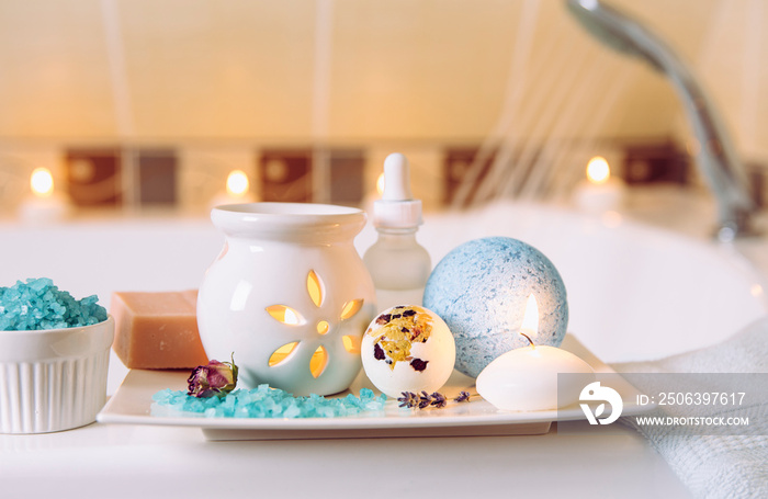 Home spa products on white ceramic tray: bar of soap, bath bomb, aroma bath salt, essential and mass