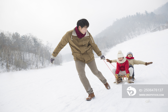 年轻的父亲和儿女在雪地上玩雪橇