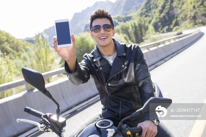 年轻男子骑在摩托车上展示手机