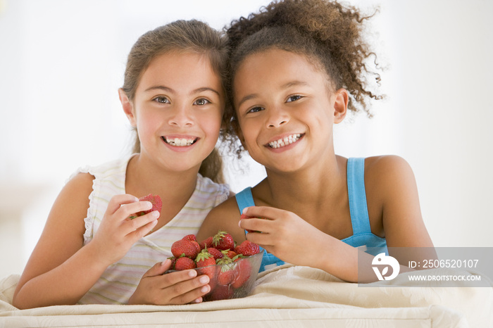 Two young girls eating strawberries in living room smiling