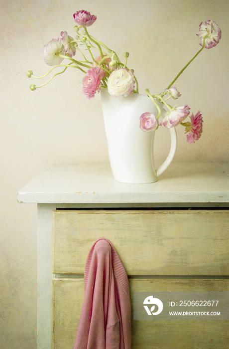 Vase of flowers and sweater on knob of dresser drawer