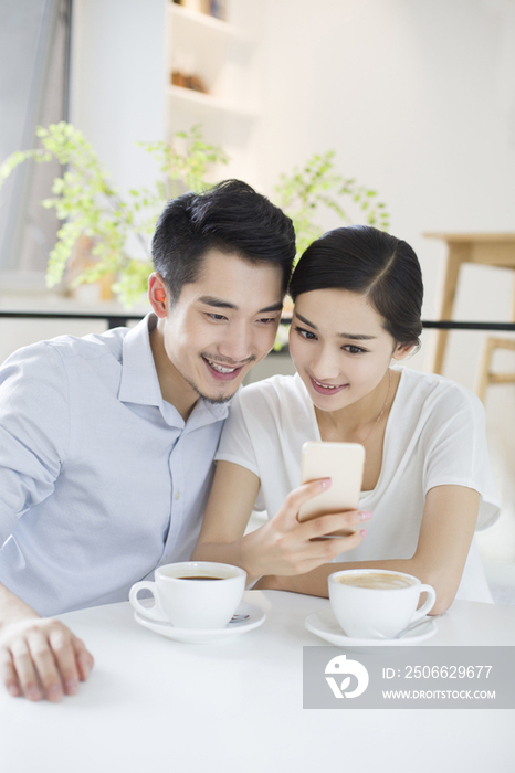 快乐的年轻情侣在咖啡店使用手机