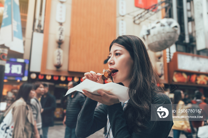 亚洲年轻女模特在日本大阪拥挤的多顿博里地区吃章鱼球饺子。当地l