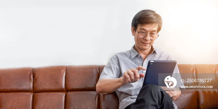 Senior Asian man playing tablet and video call on sofa in living room at home  Portrait of Asian eld