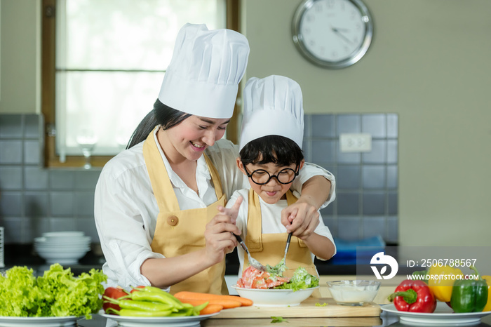 烹饪家庭。厨师小男孩和母亲为健康饮食制作和学习新鲜蔬菜沙拉