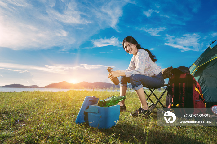 Asian woman camping and backpack travel sitting relax alone with drinks beer,water for refreshing ac