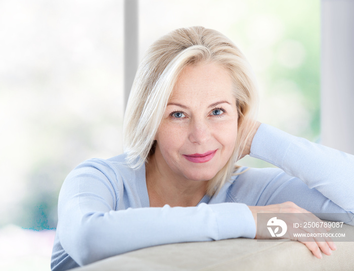 Active beautiful middle-aged woman smiling friendly and looking in camera near window at home. Woman