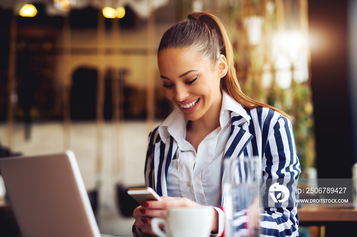 Young beautiful woman looking at smart phone at cafe bar.